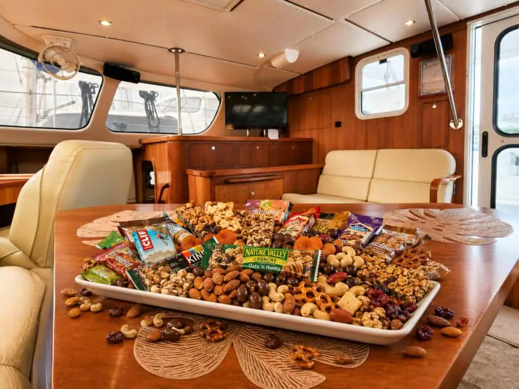 Enjoy a delicious assortment of snacks and nuts on a wooden table inside a luxurious Antares Catamaran, showcasing the comfort and elegance of the vessel's interior.
